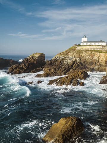Raue Küstenlinie mit Leuchtturm im Hintergrund, Asturien, Spanien, lizenzfreies Stockfoto