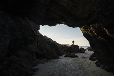 Silhouette eines Mannes, der auf einem Felsen am Eingang einer leeren Strandhöhle steht, Asturien, Spanien - JMPF00853