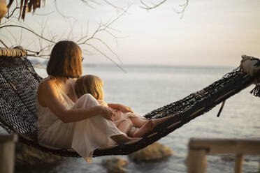 Serene mother and daughter in hammock enjoying ocean sunset - FSIF05583