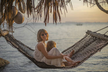 Portrait mother and daughter in hammock enjoying ocean sunset - FSIF05585