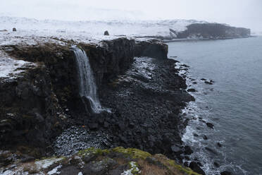 Majestätischer schneebedeckter Wasserfall über einer Meeresklippe, Arnastapi, Island - FSIF05589