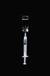Syringe in COVID-19 vaccine vial on black background - FSIF05593