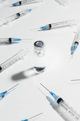 Spritzen, die die COVID-19-Impfstoffampulle umgeben, auf weißem Hintergrund - FSIF05599