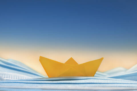 Yellow origami boat on blue disposable face mask stock photo