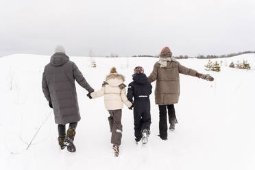 Eltern mit Kindern spazieren auf schneebedeckter Landschaft gegen den Himmel - EYAF01462