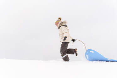 Girl pulling sled while walking on snow covered land against sky - EYAF01466