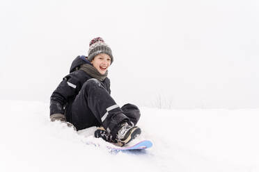 Fröhlicher Junge beim Schlittenfahren auf einem schneebedeckten Hügel - EYAF01467