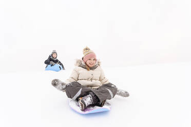 Playful siblings sledding on snow covered hill - EYAF01473