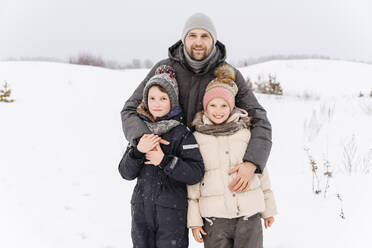 Lächelnder Vater mit Kindern in einer verschneiten Landschaft vor dem Himmel - EYAF01480