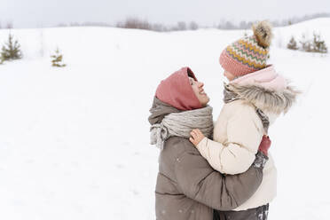 Smiling mother embracing daughter on snow covered landscape - EYAF01482