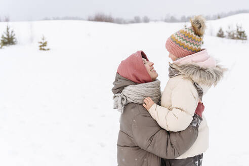 Lächelnde Mutter, die ihre Tochter in einer verschneiten Landschaft umarmt - EYAF01482