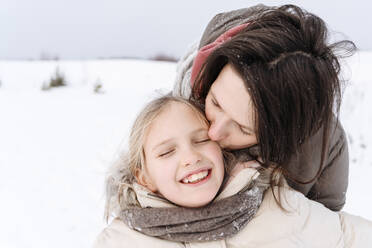 Nahaufnahme einer Mutter, die ihre lächelnde Tochter im Winter küsst - EYAF01483