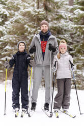 Vater und Kinder beim Skifahren gegen Bäume im verschneiten Wald - EYAF01487