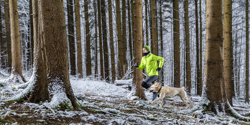 Young male sportsperson running with labrador during winter in forest - STSF02778