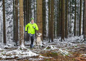 Young male athlete jogging with Labrador during winter in forest - STSF02780