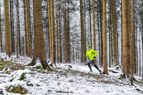 Junger männlicher Sportler joggt bei verschneitem Wetter im Wald - STSF02782