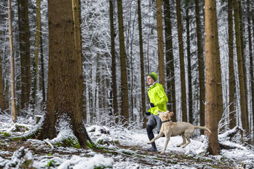 Young sportsman running with his dog during winter in forest - STSF02783