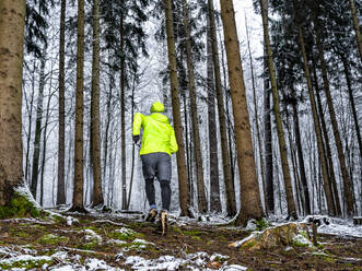 Männlicher Sportler, der im Winter im Wald zwischen den Bäumen läuft - STSF02785