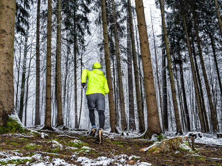 Männlicher Sportler, der im Winter im Wald zwischen den Bäumen läuft - STSF02785