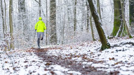 Junger männlicher Sportler in grüner Sportkleidung beim Joggen im Wald im Winter - STSF02791