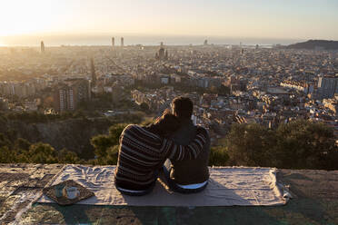 Mann, der seinen Kopf auf der Schulter seines Freundes ruht, während er das Stadtbild gegen den klaren Himmel betrachtet, Bunkers del Carmel, Barcelona, Spanien - VEGF03620
