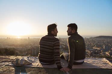 Homosexuelles Paar, das sich während des Sonnenaufgangs auf dem Aussichtspunkt sitzt, Bunkers del Carmel, Barcelona, Spanien - VEGF03621