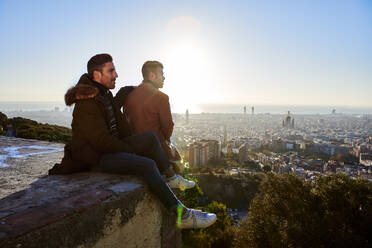 Boyfriends looking at cityscape while sitting on observation point during sunrise, Bunkers del Carmel, Barcelona, Spain - VEGF03625