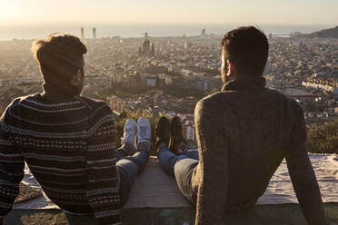 Homosexuelles Paar, das auf einem Aussichtspunkt mit Blick auf die Stadtlandschaft sitzt, Bunkers del Carmel, Barcelona, Spanien - VEGF03627