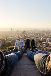 Gay couple wearing shoes sitting on observation point with view of cityscape, Bunkers del Carmel, Barcelona, Spain - VEGF03628