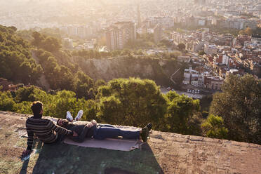 Mann ruht sich auf dem Schoß seines Freundes an einem Aussichtspunkt in der Stadt aus, Bunkers del Carmel, Barcelona, Spanien - VEGF03635