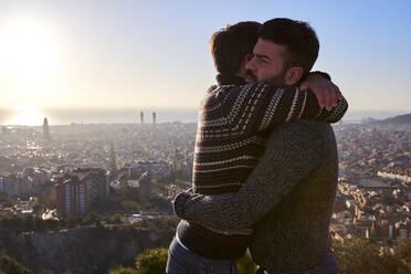 Schwule Freunde, die sich umarmen, während sie bei Sonnenaufgang vor dem Stadtbild stehen, Bunkers del Carmel, Barcelona, Spanien - VEGF03641