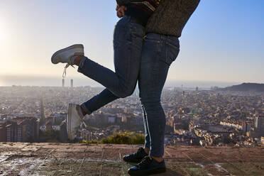 Beine von Freunden, die auf einem Aussichtspunkt stehen, mit Stadtbild im Hintergrund, Bunkers del Carmel, Barcelona, Spanien - VEGF03643