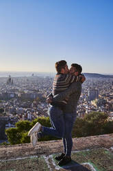 Homosexuelles Paar, das sich küsst, während es auf einem Aussichtspunkt gegen den klaren Himmel steht, Bunkers del Carmel, Barcelona, Spanien - VEGF03644