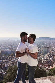 Schwule Männer, die sich umarmen, während sie an einem sonnigen Tag vor einer Stadtlandschaft stehen, Bunkers del Carmel, Barcelona, Spanien - VEGF03661