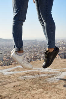 Beine von schwulen Männern, die auf einem Aussichtspunkt gegen den klaren Himmel in der Stadt springen, Bunkers del Carmel, Barcelona, Spanien - VEGF03664