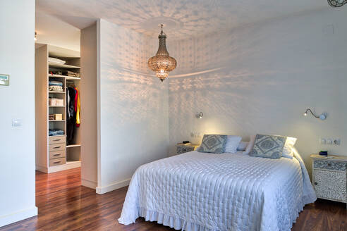 Interieur eines gemütlichen Schlafzimmers mit großem weißen Bett und klassischem Kronleuchter an der Decke - ADSF20307