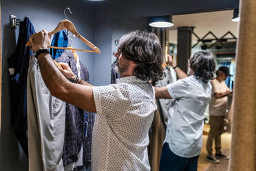 Seitenansicht eines Mannes beim Anprobieren von Kleidung in der Umkleidekabine eines Bekleidungsgeschäfts - ADSF20319