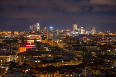 Blick auf die Stadt Madrid mit Wohngebäuden mit beleuchteten Fenstern bei Nacht unter einem dunklen bewölkten Himmel - ADSF20343