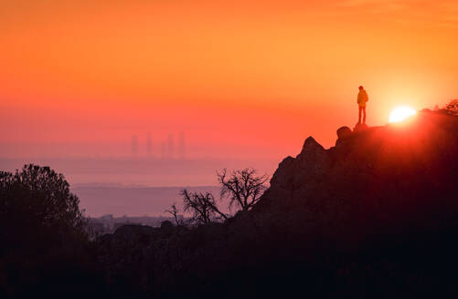 Remote view of unrecognizable tourist standing on rock and enjoying view of Madrid at sundown - ADSF20347