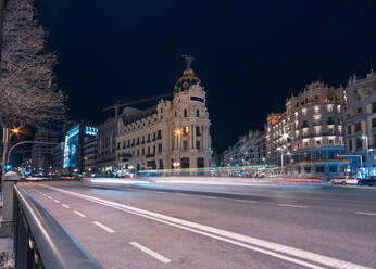 Berühmtes Metropolis-Gebäude in der Nähe einer Straße, beleuchtet von unscharfen Ampelspuren in Madrid - ADSF20353