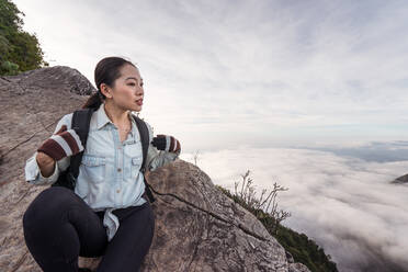 Ethnische Wanderin sitzt auf einem Stein im Hochland und bewundert die atemberaubende Aussicht auf den Yuanzui-Berg während einer Reise - ADSF20379