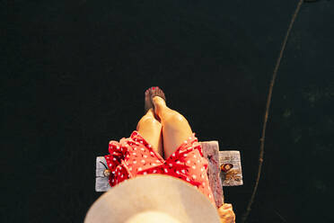 Frau mit Hut sitzt mit dem Bein im Wasser am Rande des Piers - DGOF01841