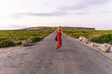 Carefree woman with arms outstretched spinning while standing on road - DGOF01853