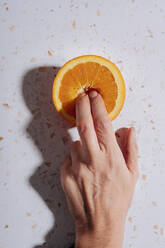 Finger einer Frau in halbierter Orange auf modernem Terrazzomarmor - GEMF04591