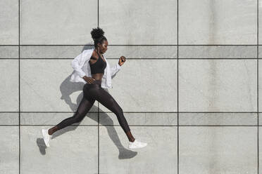 Side view of fit African American female athlete jumping above ground on street while doing exercises during workout - ADSF20400