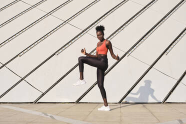 Side view of focused ethnic sportswoman doing exercises and warming up legs while looking at camera during dynamic workout - ADSF20403