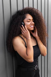 Lovely African American female with long curly hair and headphones in city and closed eyes - ADSF20472