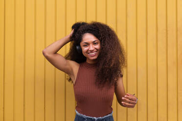 Hübsche Afroamerikanerin mit langen lockigen Haaren und Kopfhörern in der Stadt und mit Blick in die Kamera - ADSF20478