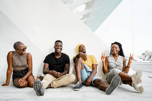 Gruppe positiver, freundlicher afroamerikanischer Menschen in stilvoller Kleidung, die auf dem Boden in einem städtischen Gebiet in der Stadt sitzen - ADSF20490