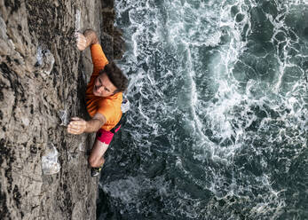 Passionate male rock climber climbing rocky cliff by sea - ALRF01814